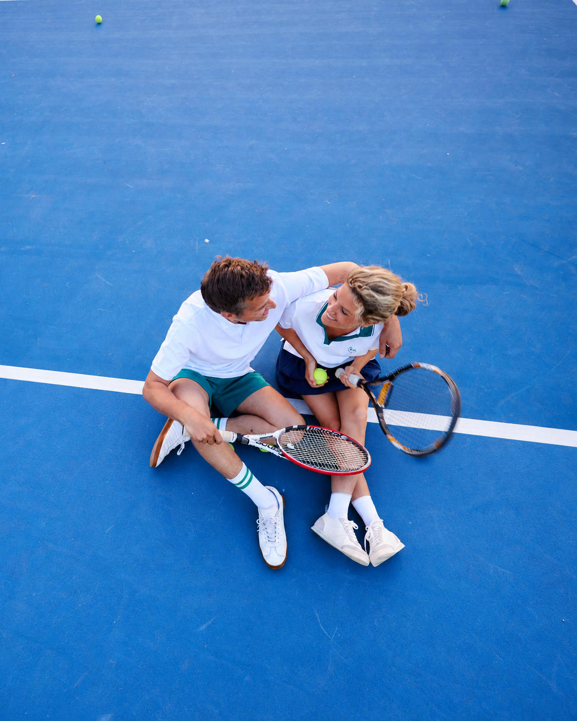 Zwei Padel-Spielende sitzen lachend auf einem blauen Court